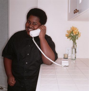 Teenage boy (16-17), talking on telephone in home, portrait
