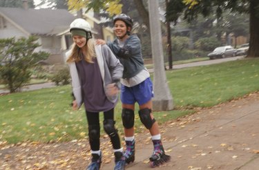 Two teenage girls (14-15) inline skating in park