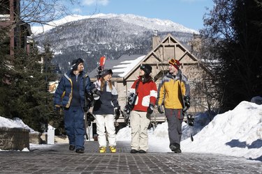 Four adults with skis and snowboards walking and talking