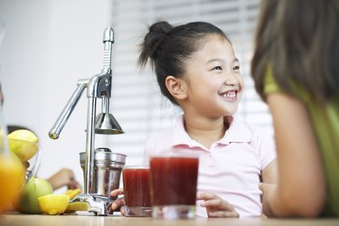 Girl (5-7) in kitchen grinning by juice