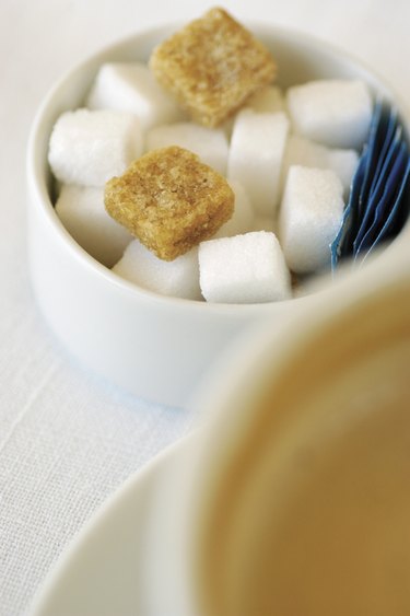 Sugar bowl with sugar cubes next to cup of cappuccino