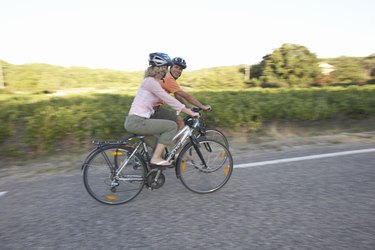 Woman and man riding bicycles on country road, side view