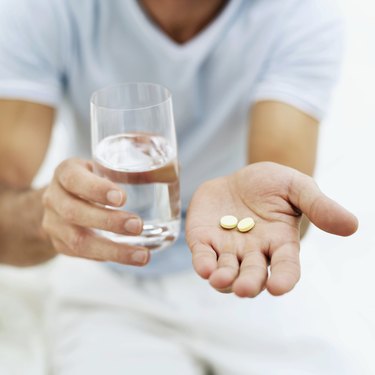 close-up of a person holding pills and a glass of water