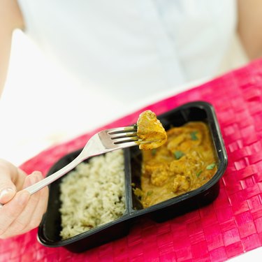 Close-up of a woman's hand eating chicken curry with a fork