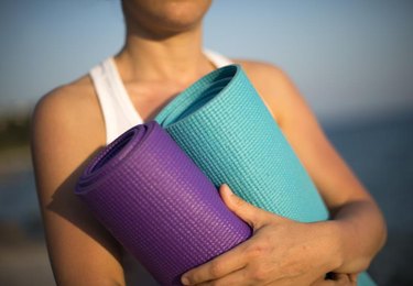 Unrecognised lady holds two yoga mats in natural backround.