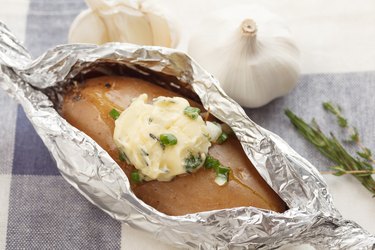 High-calorie baked potato cooked in aluminum foil and topped with butter, garlic and herbs.