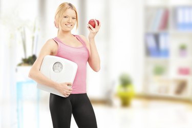 Young smiling female holding a weight scale and an apple