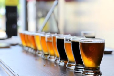 Craft beers in taster glasses are lined up on a bar counter for a beer tasting.