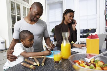 Father and son (6-7) drawing at kitchen counter, mother using mobile phone