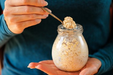 Woman's slender hands holding glass jar and spoon with overnight