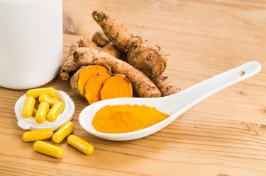 Turmeric spice powder and supplement pills next to fresh sliced turmeric root.