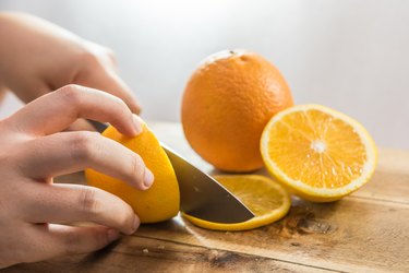 Hand slicing orange on wooden board