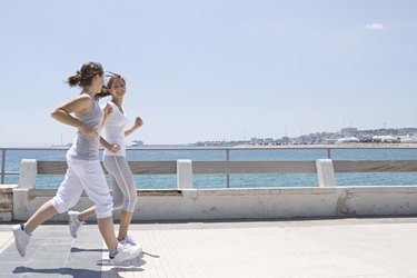Teenage girls running on sidewalk by ocean