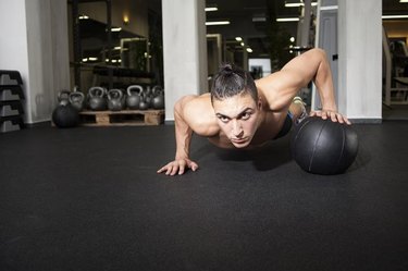 Athlete performing one-handed push up on a medicine ball at the gym.