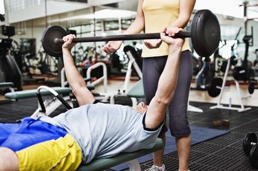 Woman spotting man lifting barbell