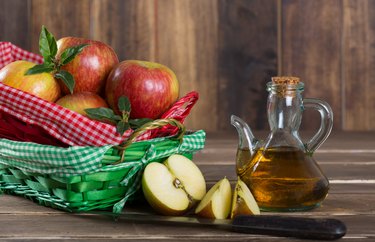 Apple Cider Vinegar next to a basket of apples on a wooden backdrop.