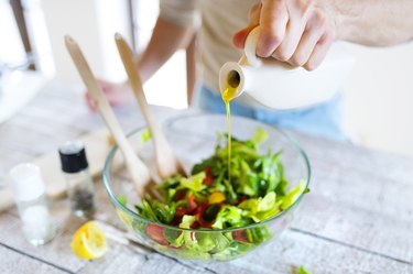 hand pouring olive oil into salad on wooden table