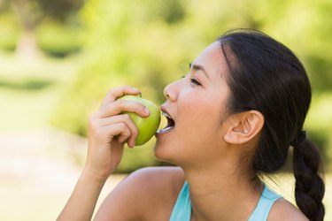 Healthy young woman eating apple in park