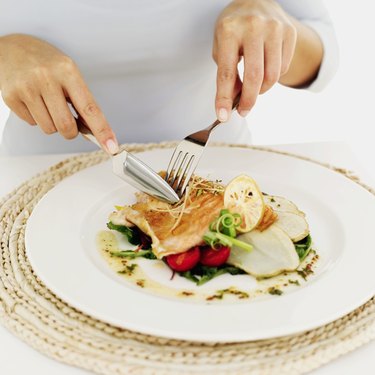 person using a fork and knife on a plate of grilled salmon