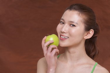 Young woman holding a apple and getting ready to take a bite, looking at camera, studio shot