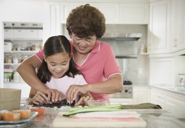 Asian grandmother teaching granddaughter to make sushi hand roll