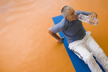 Man sitting on exercise mat, drinking water