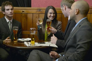 Businesswoman having drinks with three male colleagues in bar, smiling