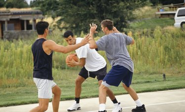 Three teenage boys (16-17) playing basketball on outdoor court