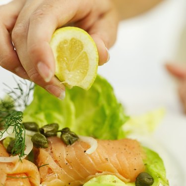 close-up of a person's hand squeezing lemon on a sushi salad