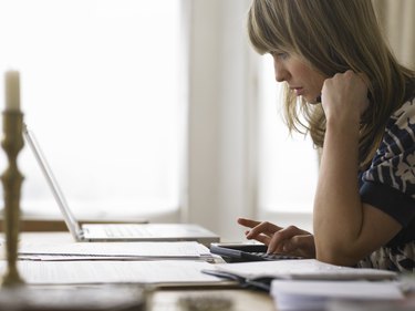 Young woman looking at laptop while using calculator