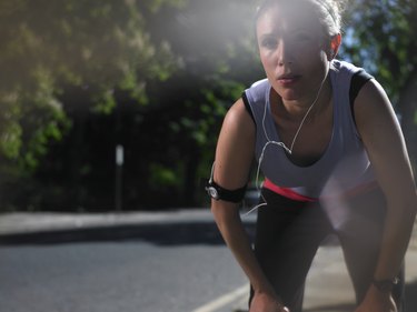 Young woman at street breathing heavily after jogging, lens flare