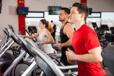 Profile view of a couple of men and a woman doing some cardio on a treadmill in a gym