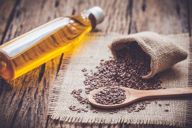 Flax seeds in the sack and oli on wooden background