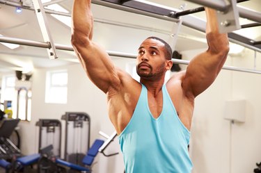 Muscular man flexing muscles on monkey bars at a gym