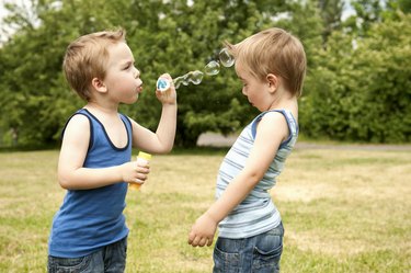 Twin blowing bubbles at brother in park