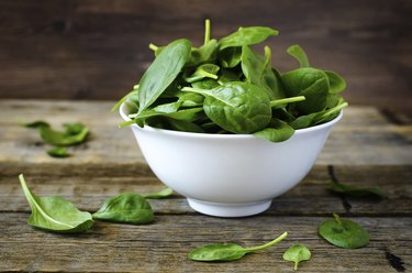 A bowl of spinach on a wooden table.