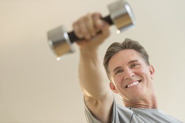 Happy Man Lifting Dumbbell Against Beige Background