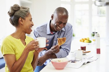 Couple Having Breakfast And Reading Magazine In Kitchen