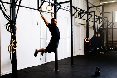 Young man doing kipping pull-ups exercise at gym