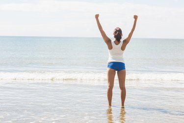Lovely slim woman standing on beach raising her arms