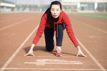 Athletic Asian woman in start position on track
