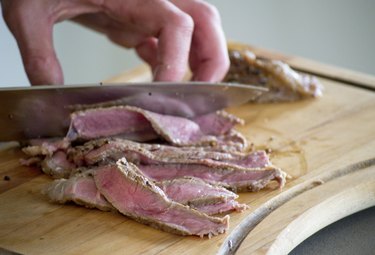 close up image of a hand cutting sirloin steak into thin slices on a cutting board with a sharp knife