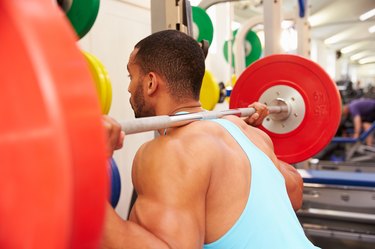 Man weightlifting barbells at a squat rack in a gym