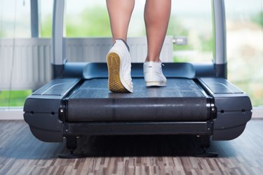 Fitness girl running on treadmill. Woman with muscular legs in