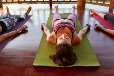 Shot of women at yoga class doing savasana, lying on exercise mat. Young people relaxing at yoga class.