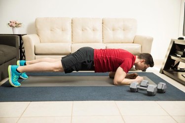 Full length profile view of an athletic man exercising and doing a plank at home