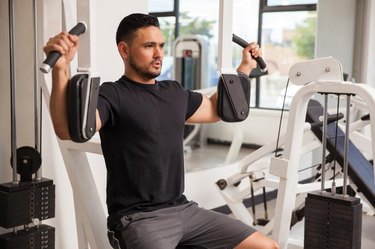 Good looking young man building muscle at the gym using a pec deck machine