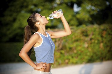 Slim young woman drinking water after training