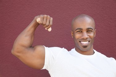 Portrait of a young African American man flexing muscles over colored background