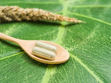 Two supplement capsules on a wooden spoon on top of a large green leaf